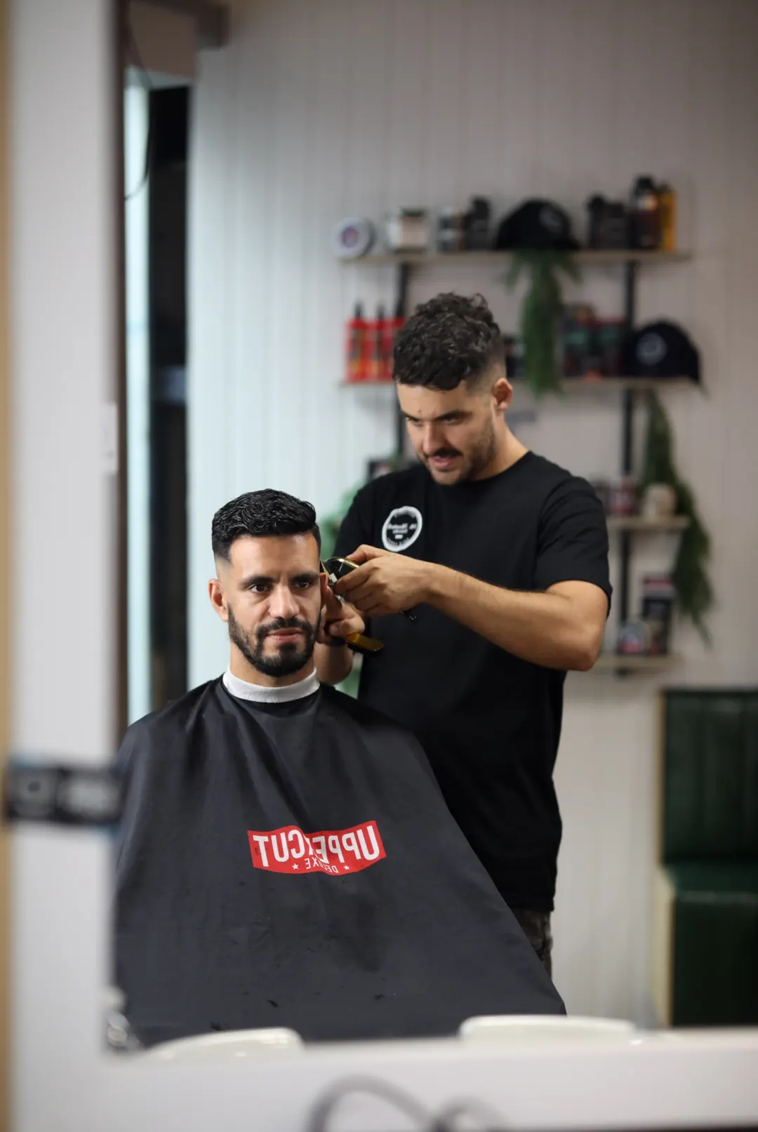 Mr Moustache barber lining up a client's beard, seen in the shop mirror
