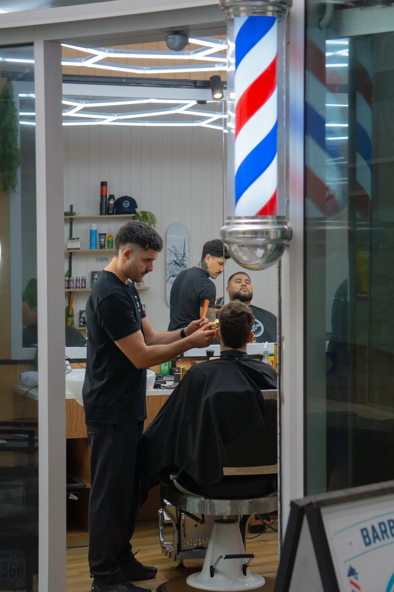 Mr Moustache barber cutting a client's hair beside the barber pole